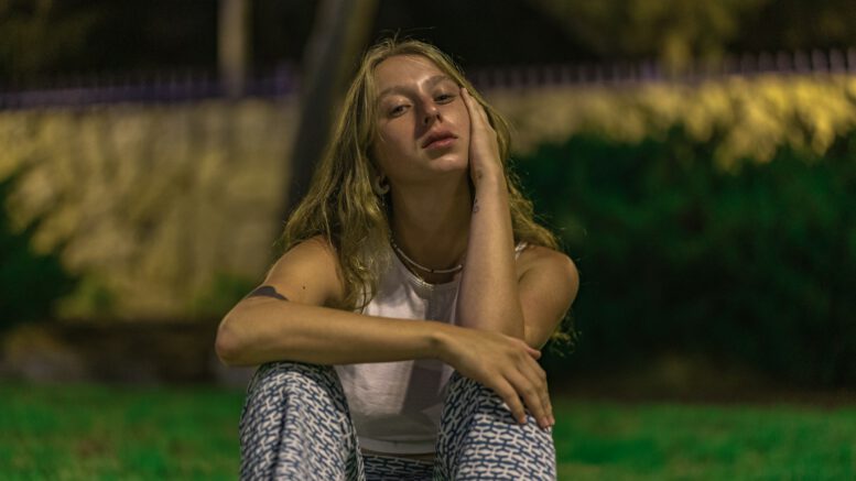 woman in white tank top and black and white pants sitting on green grass during daytime